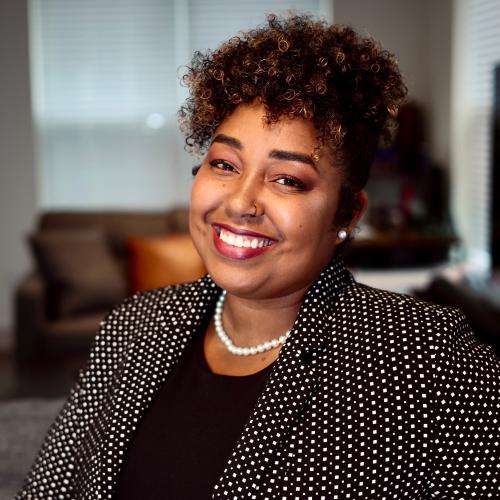 Chest-high picture of Lora sitting at a counter with a black and white blazer and black shirt