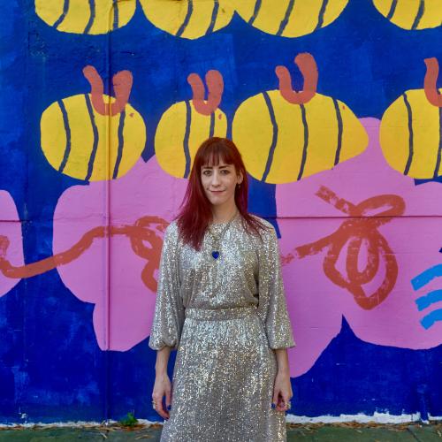 white woman wearing sequin dress and standing in front of a brightly colored mural