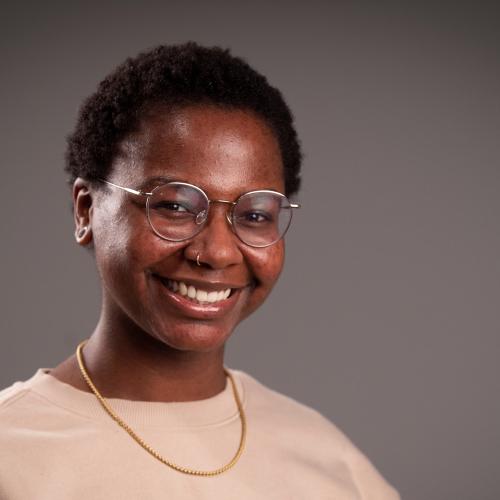 Amber D. Dodd is wearing a gold chain and tan sweater and smiling for her professional headshot