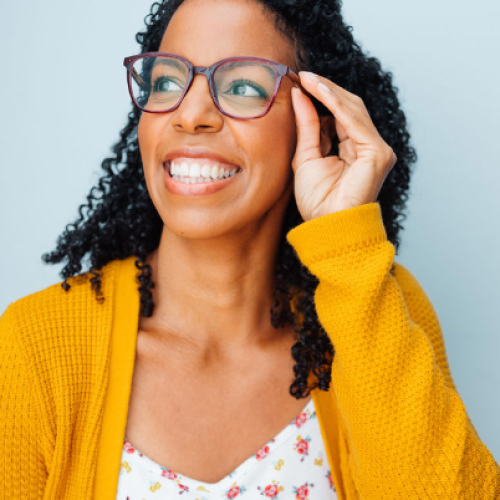 Afro-Latina woman wearing red glasses and a yellow cardigan looking up away from the camera and smiling