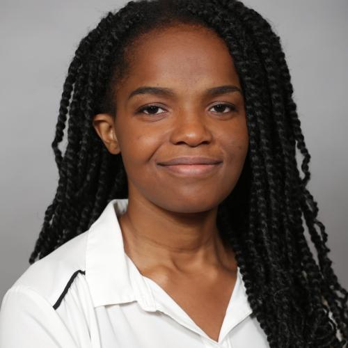 Headshot of Shayla smiling slightly in a white button down shirt in front of a gray background