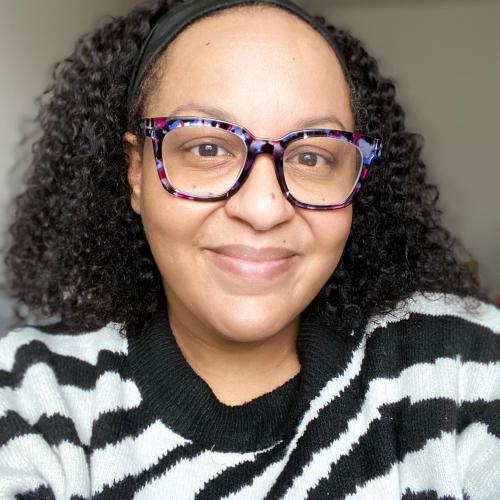 A picture of Dr. Jaye Nias wearing a black and white patterned sweater and colorful glasseson a neutral background.