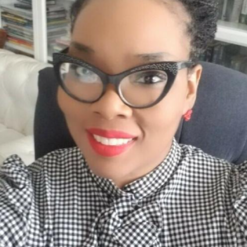 Christina Vortia is pictured wearing black cat lady glasses, red lip earrings, and bright red lipstick.