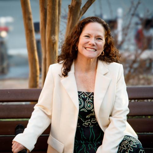Samatha Powers in a white blazer, sitting on a park bench