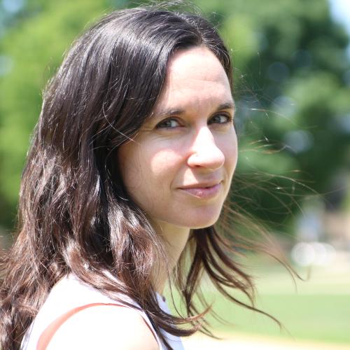 Headshot image of a white woman with brown hair and greenery in background.