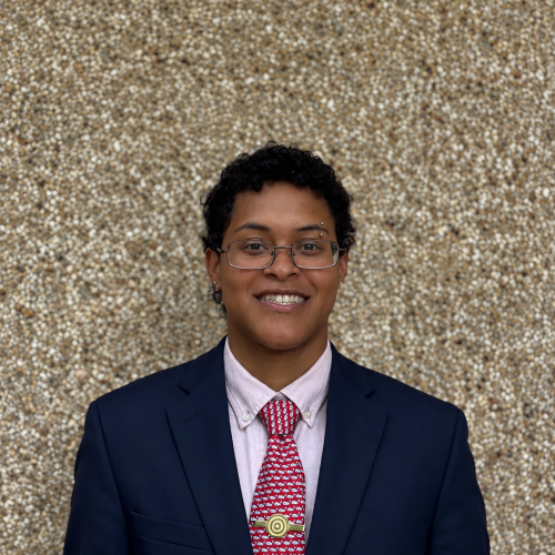 Young man with a round face and rectangular wire glasses. Blue suit, red tie with whales on it